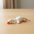 White articulated flexi goose keychain lying flat on wooden desk
